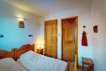 A cozy bedroom featuring two wooden single beds with white bedding, a wooden nightstand with a lamp, and two matching wooden doors. Minimal wall decor.