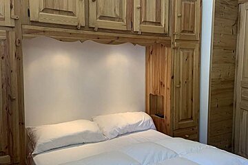 A bedroom with wooden cabinets and a bed with white sheets