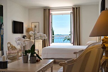A luxurious room with elegant decor, white orchids, and open balcony doors showcasing a breathtaking sea view.
