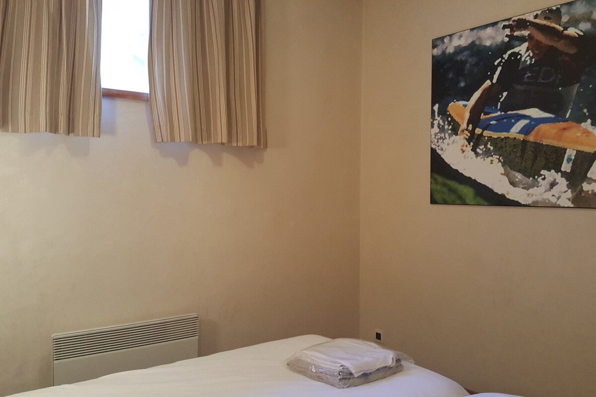 A room with a bed, striped curtains, a heater, and a large picture of a surfer or wakeboarder on the wall.