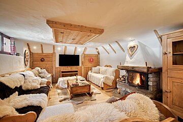 Warm, rustic ski chalet living room with a cozy fireplace, wood paneling, fur throws, and a TV.