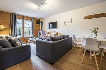 Cozy cabin living room featuring grey sofas, a small dining area, wooden floors, and a wood stove.