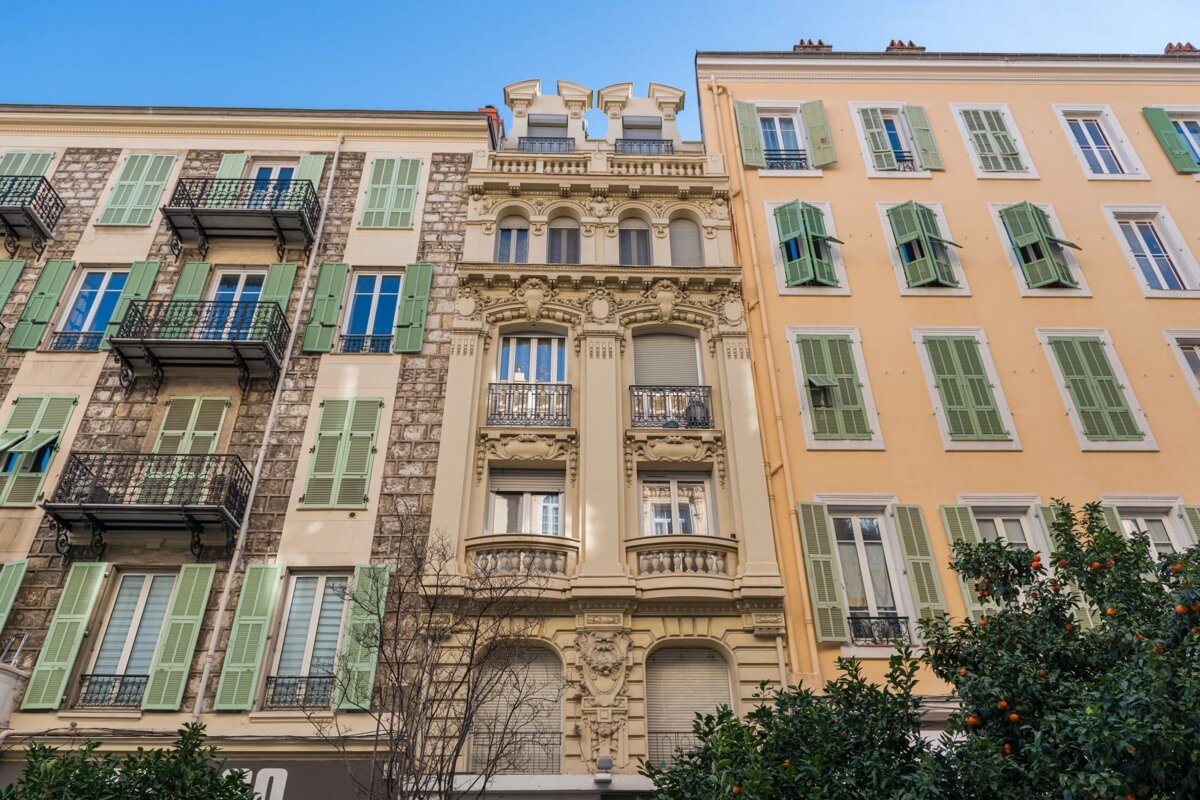 Low-angle view of colorful European-style apartment buildings with green shutters under a blue sky.