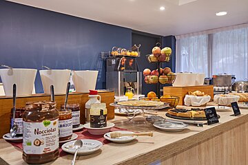 A self-serve breakfast buffet with jars of spread, fresh fruit, juice, crepes, and pastries, set against a blue wall.