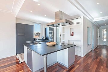 Bright, modern kitchen with a large island, dark gray cabinets, stainless steel appliances, recessed lighting, and warm hardwood floors.