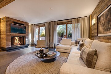 Modern rustic living room with a warm fireplace, large TV, white sectional sofa, wood walls, and big windows.