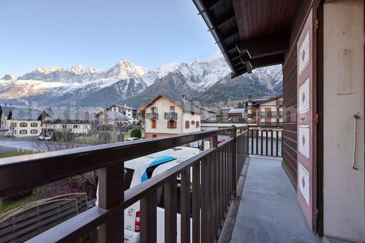 Balcony view of a charming mountain village with snow-capped peaks towering in the distance under a clear sky.