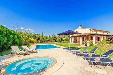 Sunny villa with two pools, multiple lounge chairs, and lush greenery under a clear blue sky, perfect for a relaxing getaway.