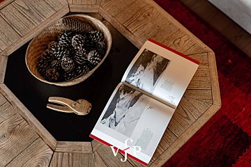 An open book, a basket of pine cones, and a carved wooden nutcracker on an octagonal coffee table.