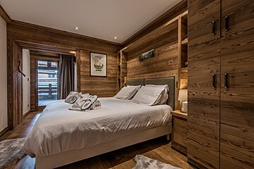 A bedroom with wooden walls and a bed with white sheets