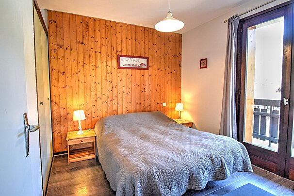 Cozy bedroom with a double bed, wood-paneled wall, bedside lamps, and a door leading to a balcony.