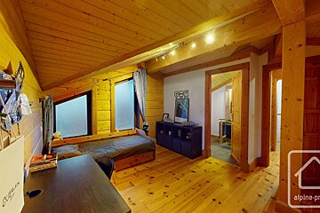 Cozy all-wood room with sloped ceiling, bed, desk, and storage. Multiple doorways open to other spaces, all in warm wooden tones.