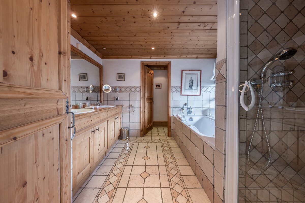 Rustic bathroom featuring wooden cabinetry and ceiling, a tiled bathtub, patterned floor tiles, and a shower in the foreground.