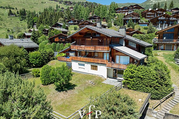 Beautiful wooden chalets on a lush green mountain hillside on a sunny day.