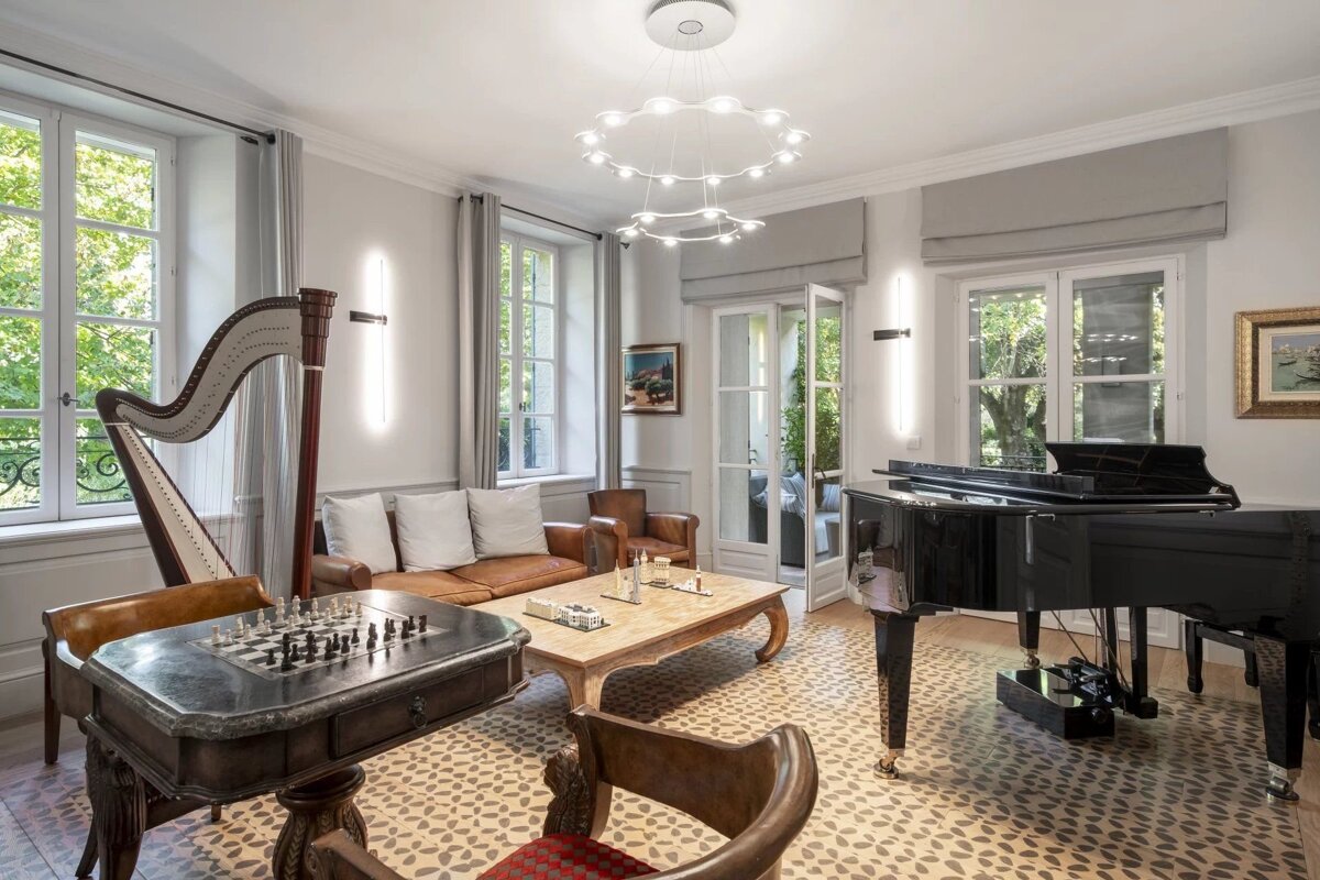An elegant living room featuring a grand piano, a harp, a chess table, leather seating, and large windows.