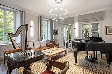 An elegant living room featuring a grand piano, a harp, a chess table, leather seating, and large windows.