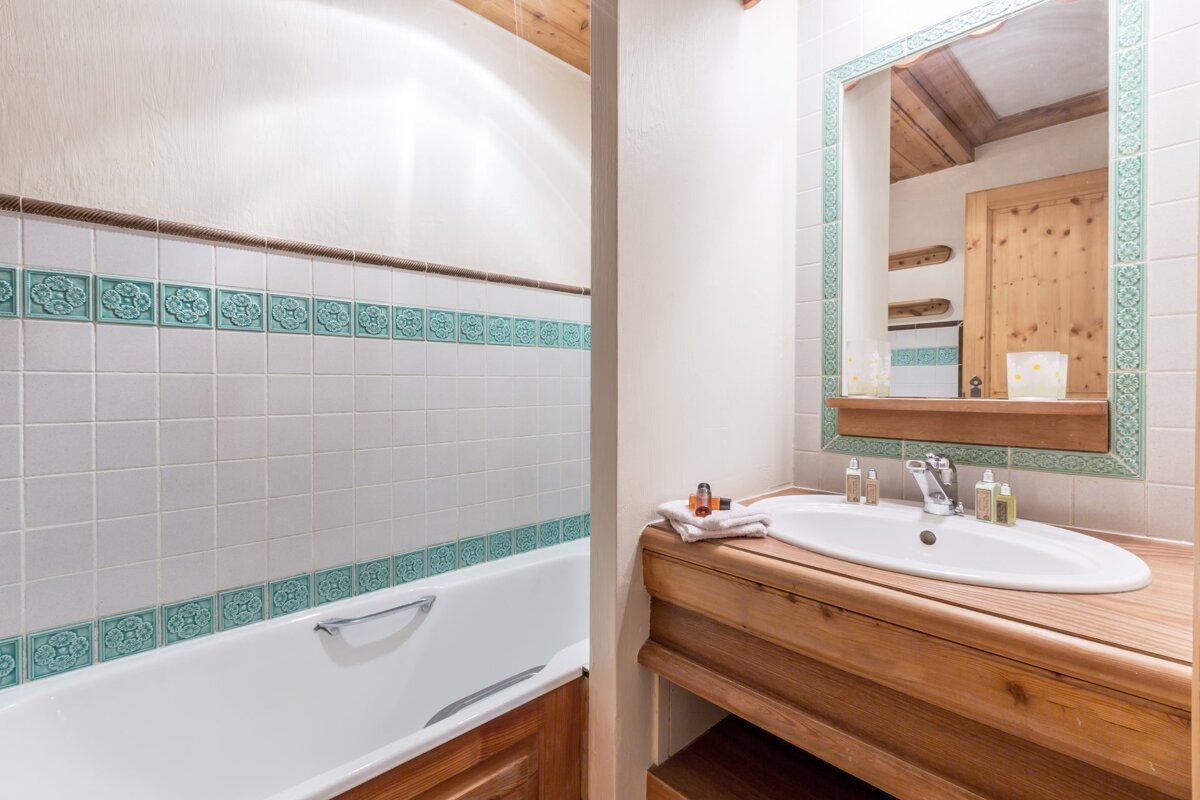 A cozy bathroom with a white tiled bathtub and teal accents, a wooden vanity with a sink, and a mirror with a decorative teal frame.