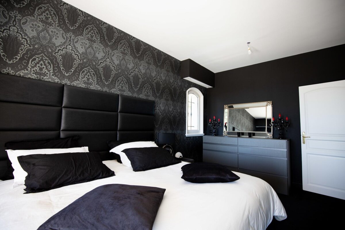 A bedroom with black walls and a bed with black pillows