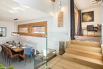 A modern split-level home interior featuring a set dining table below and a study desk upstairs, connected by wooden steps.