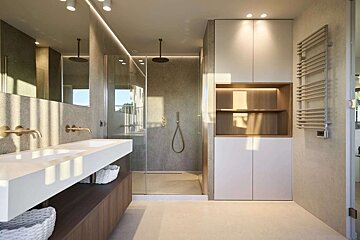 Sleek, modern bathroom with a double white vanity, bronze fixtures, a walk-in shower, and integrated storage, bathed in warm natural light.