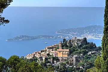 A picturesque village with a church and castle ruins perched on a cliff, overlooking the blue sea with distant islands and boats.
