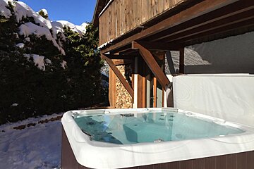 A hot tub outside of a house with snow on the ground