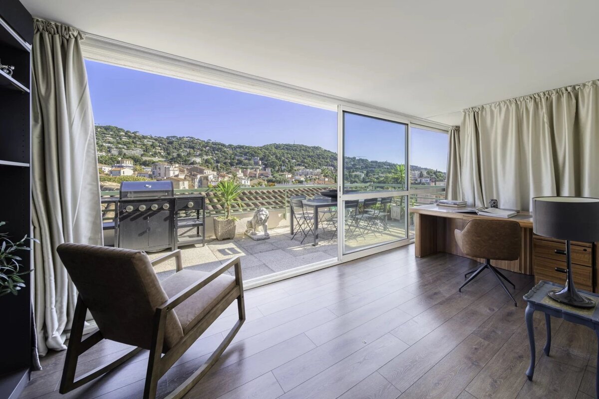 Modern room with sliding glass doors opening onto a sunny terrace with a BBQ and beautiful hillside views.