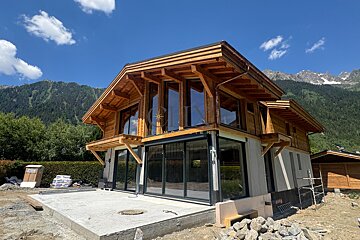 A wooden chalet-style house under construction with mountains in the background.