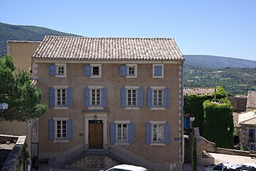 A building with blue shutters and a street sign that says rue