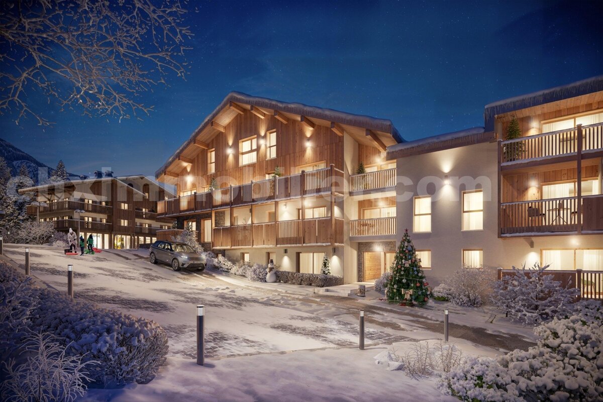 Illuminated modern chalets in a snowy mountain village at night, with a festive Christmas tree, snowman, and people sledding.