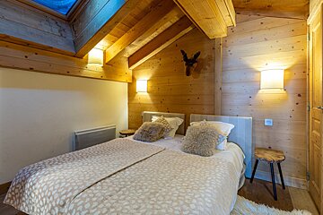 A cozy wooden chalet bedroom featuring a sloped ceiling with a skylight, a large bed with fluffy pillows, and warm wall lighting.
