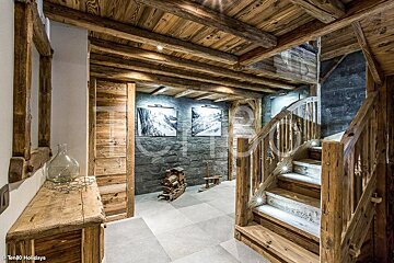 Cozy chalet interior featuring a rustic wooden staircase, exposed beam ceiling, stone accent wall, and tiled flooring.