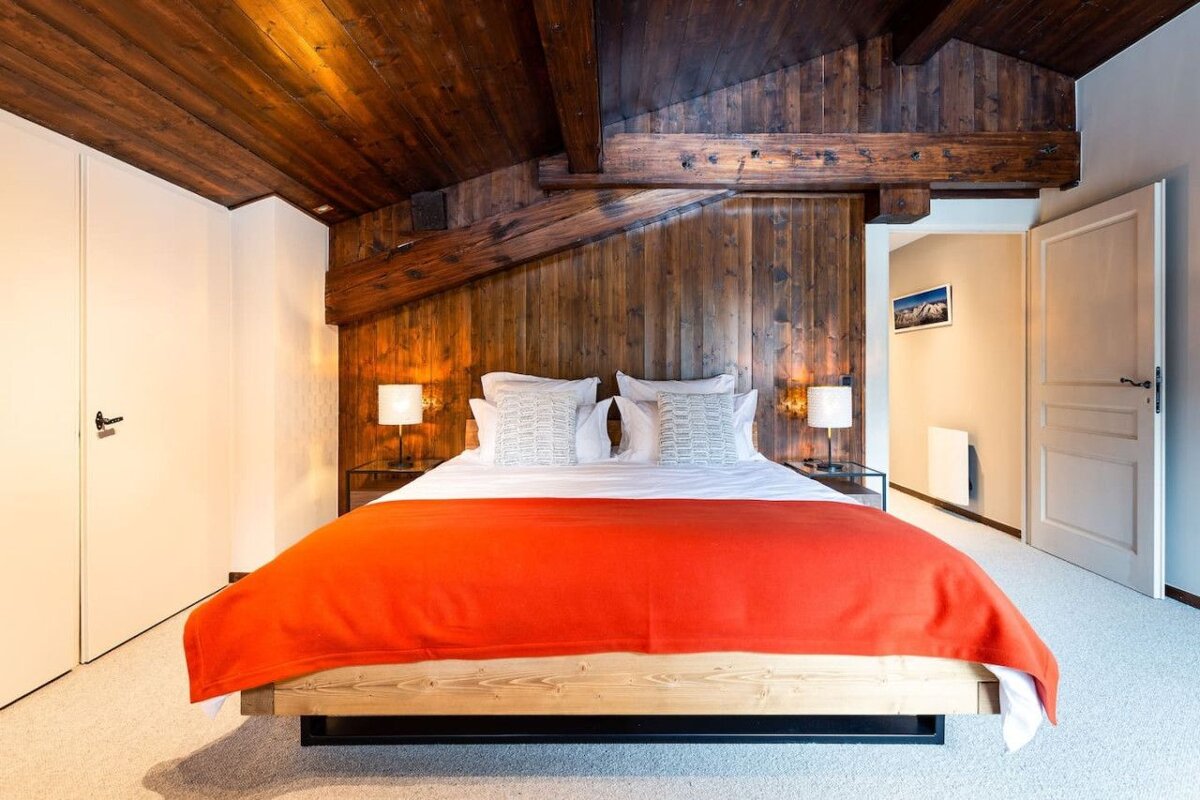 A bedroom with a wooden ceiling and a bed with an orange blanket