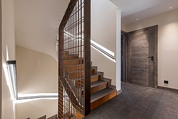 Wooden staircase with a rusted metal grid screen next to a rustic wooden door in a modern hallway with dark wood flooring.