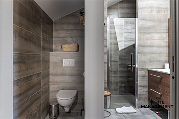 A modern bathroom with grey wood-look tiles, featuring a wall-mounted toilet, a glass shower enclosure, and a wooden vanity.