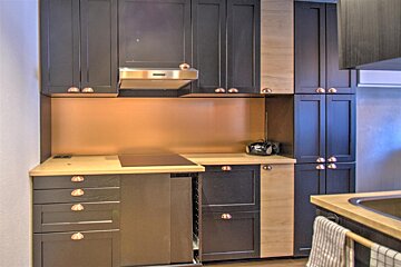 Modern kitchen with dark grey and light wood cabinets, copper handles, light wood countertops, and a copper backsplash.