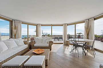 Bright sunroom with wicker furniture, white cushions, a dining table, and large glass doors offering scenic views.