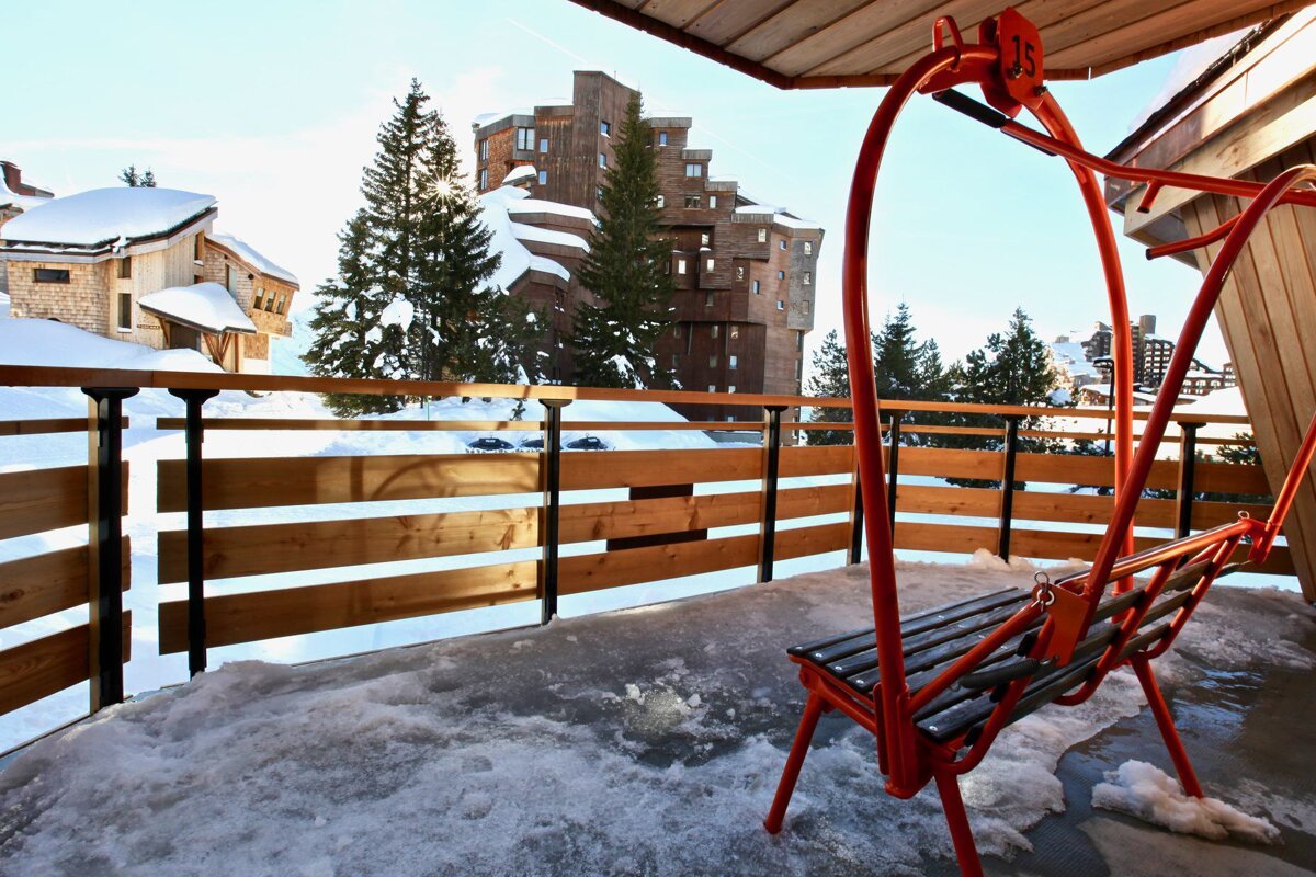 A red swing sits on a snowy balcony overlooking snow covered buildings