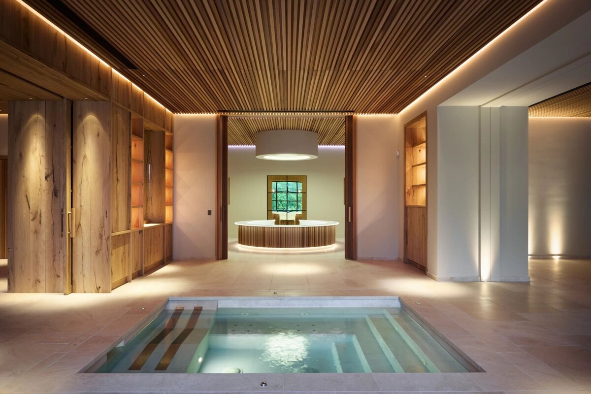 Serene indoor spa with an in-ground hot tub, warm wooden ceilings, and soft lighting, leading to a circular counter room.
