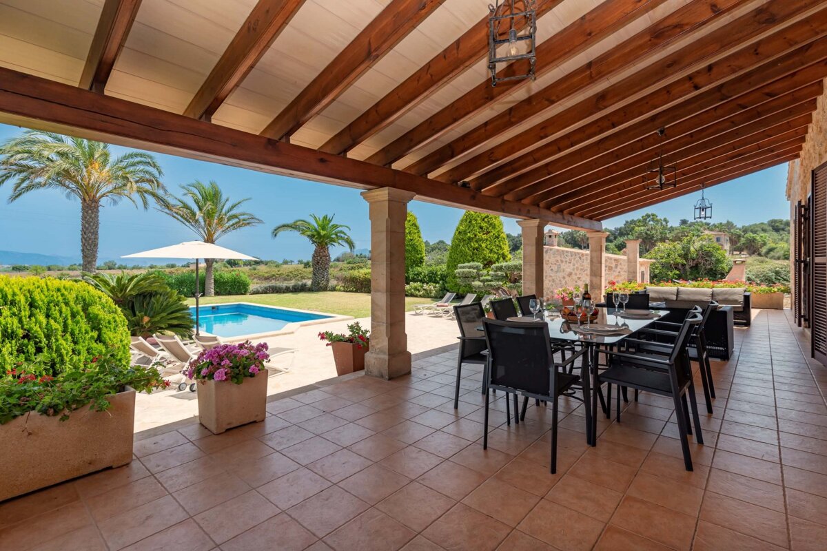 A patio with a table and chairs and a pool in the background