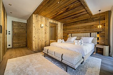 Cozy chalet-style bedroom with extensive wood paneling, a white bed, an upholstered bench, and plush rugs.