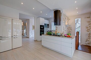 A modern kitchen with white cabinets, a black hood, and retro fridges, featuring light wood floors and stone accent walls, with fresh vegetables on the island.