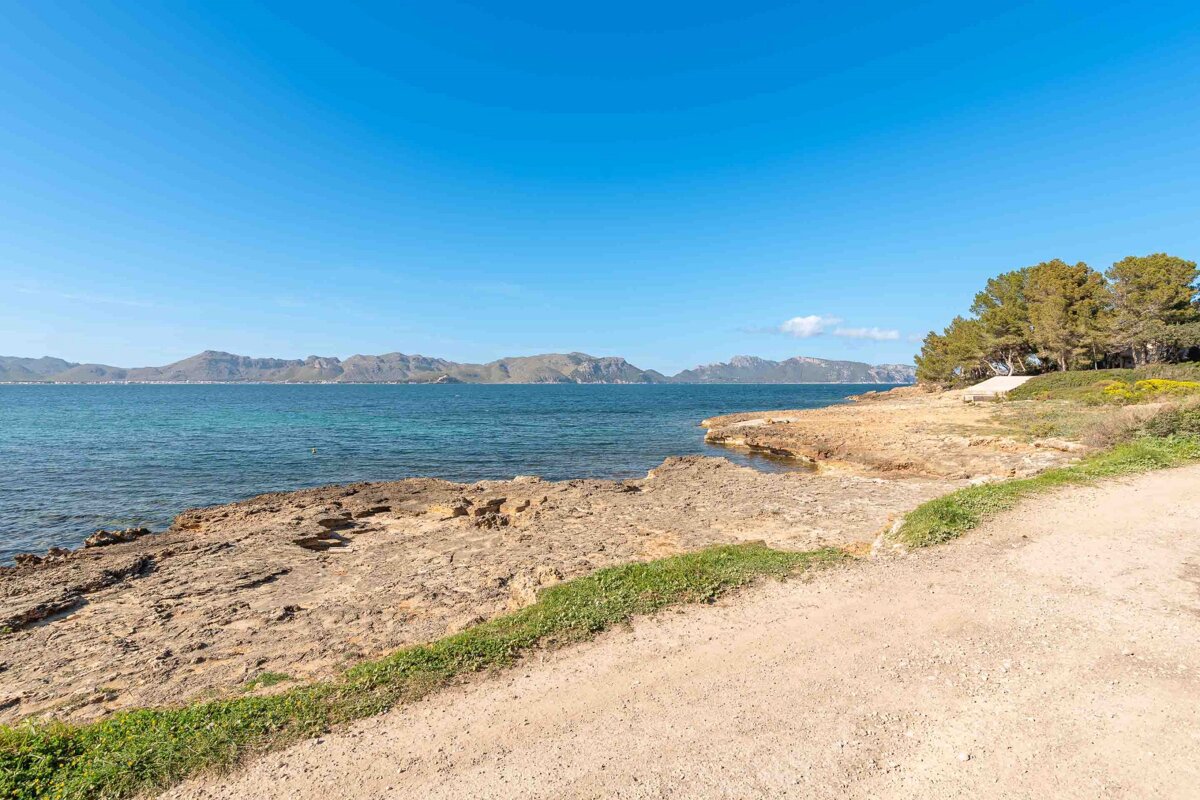 A dirt road leads to the ocean with mountains in the background