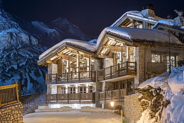 A large house with snow on the roof is lit up at night