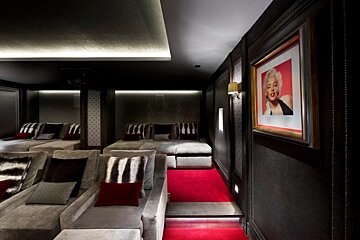 Luxurious home cinema with plush grey chaises, red carpet, dark walls, ambient lighting, and a framed Marilyn Monroe portrait.
