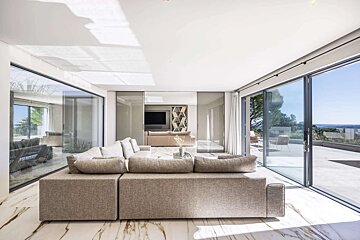 A bright, modern living room with a large sofa, marble floors, and panoramic glass doors leading to an outdoor view.