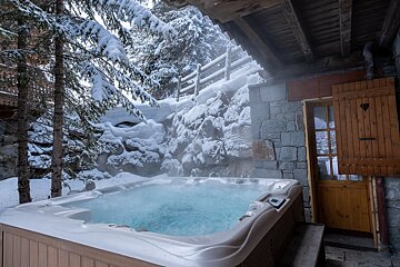 An inviting, steaming outdoor hot tub nestled in a snowy winter landscape, surrounded by frosted pine trees and a cozy stone chalet.