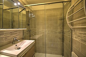 A clean, modern bathroom with a sink, illuminated mirror cabinet, and a glass-enclosed shower with beige tiling and a towel warmer.