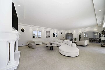 Bright, minimalist living room with a large white curved sofa, fireplace, arched windows, and light grey floor tiles.