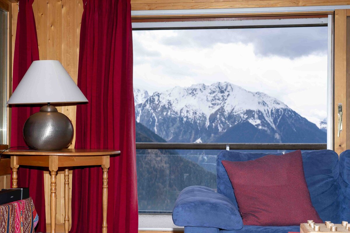 A lamp sits on a table in front of a window with mountains in the background